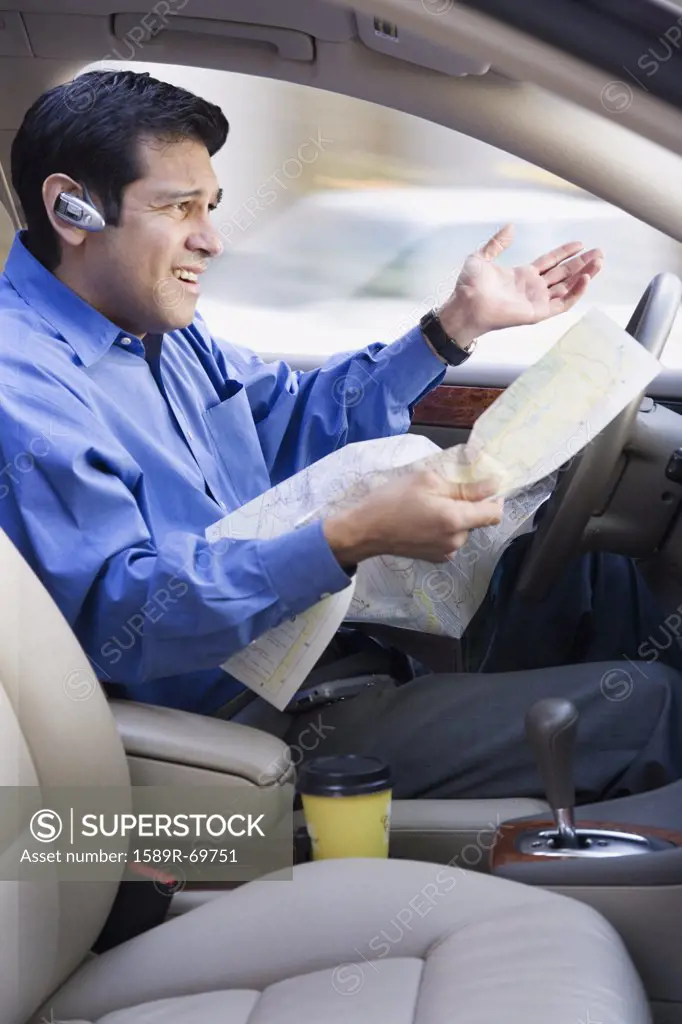 Hispanic businessman looking at map and driving