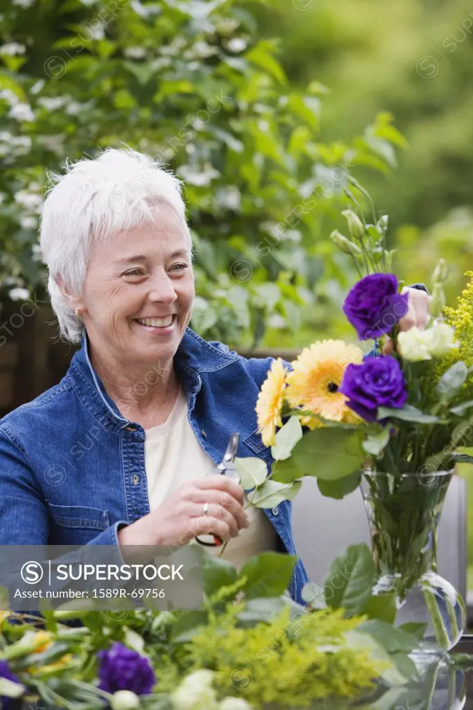 Senior woman smiling and arranging flowers in vase