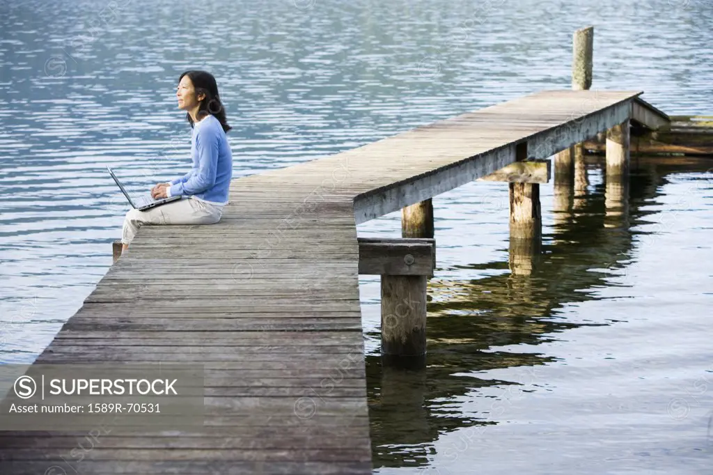 Asian woman holding laptop on edge of pier