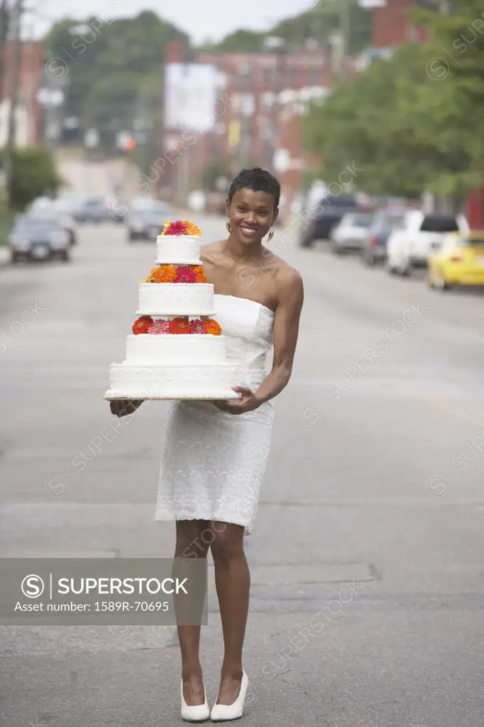 African bride holding wedding cake in street