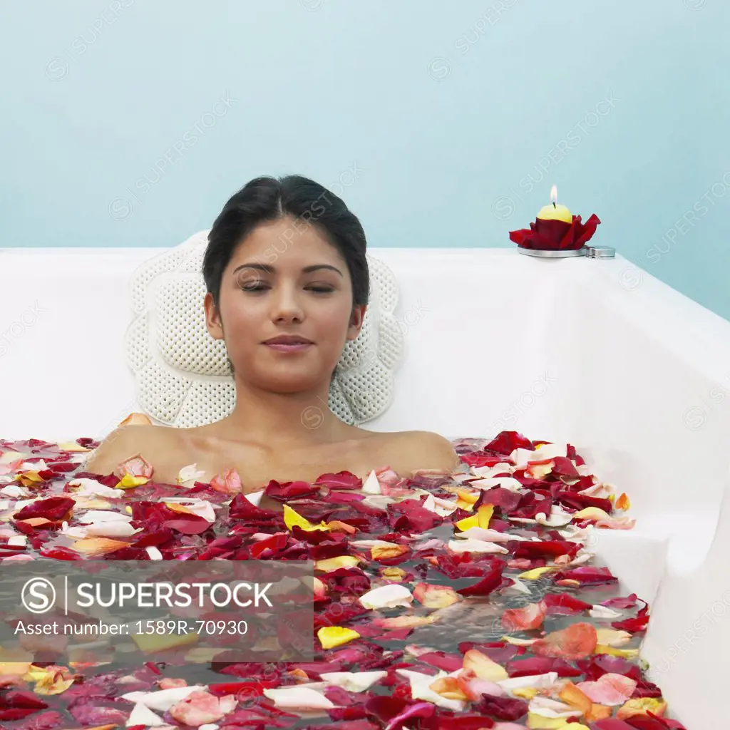 Hispanic woman in bathtub with flower petals
