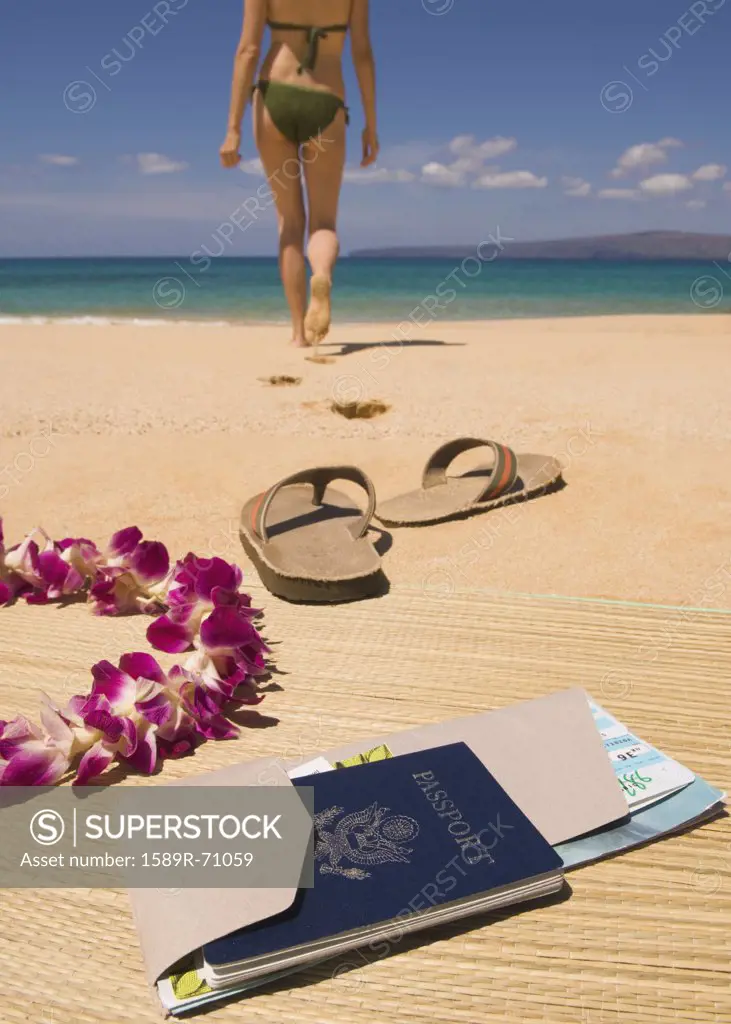 Woman walking away from passport and sandals on beach