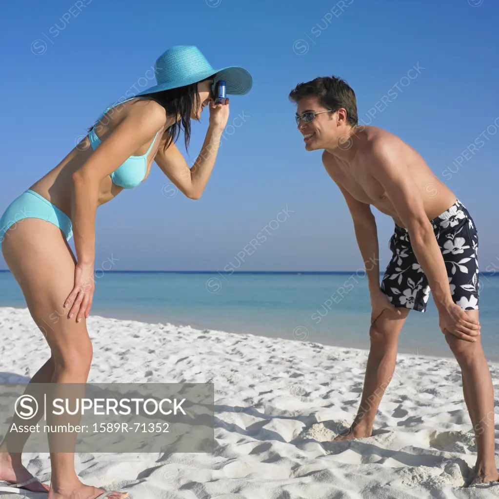 Woman taking boyfriend's photograph at beach