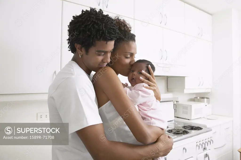 African parents hugging baby in kitchen