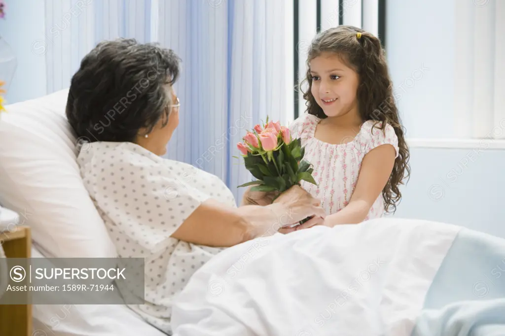 Hispanic girl giving flowers to grandmother in hospital bed