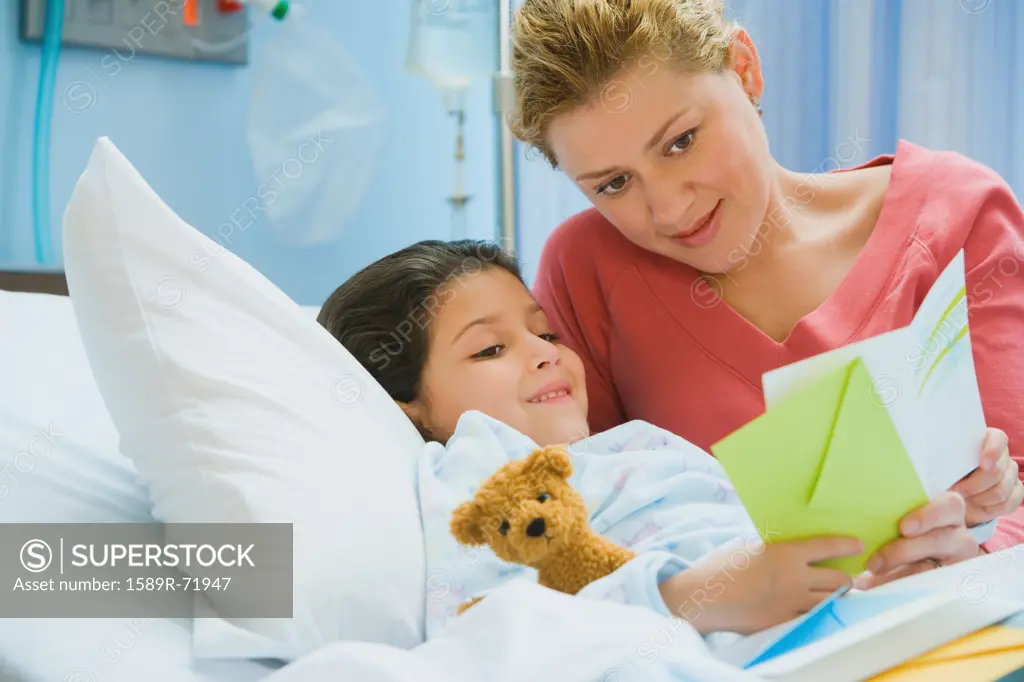 Mother reading card to daughter in hospital bed