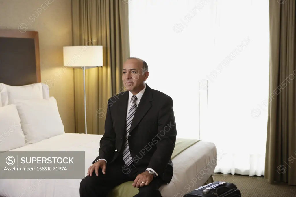 Middle-aged businessman sitting on bed in hotel room