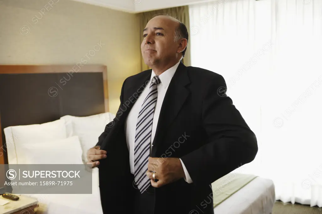 Middle-aged businessman putting on jacket in hotel room