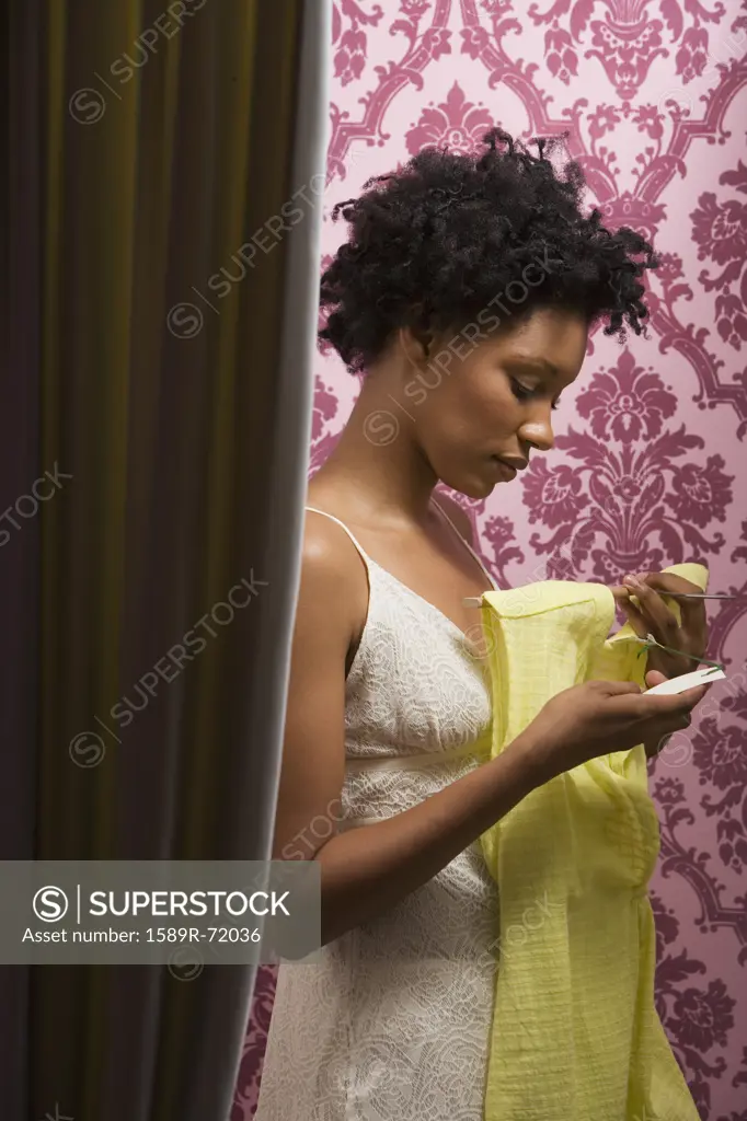 African woman looking at price tag on dress in fitting room