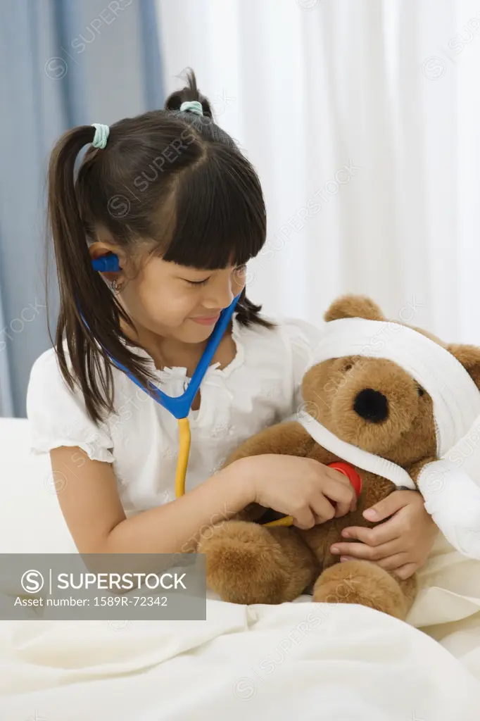 Pacific Islander girl examining teddy bear with stethoscope