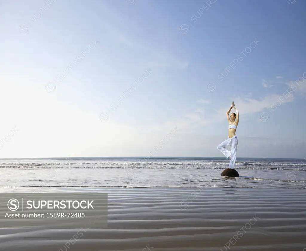 Pacific Islander woman practicing yoga at beach