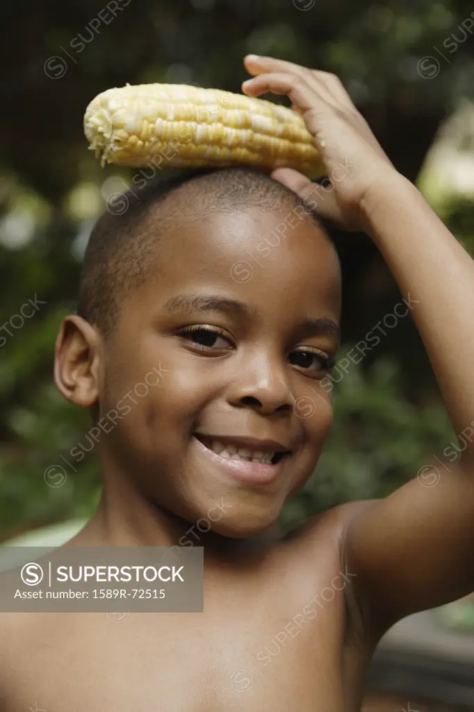 African American boy holding ear of corn on head