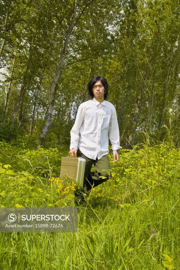 Asian man carrying briefcase in tall grass