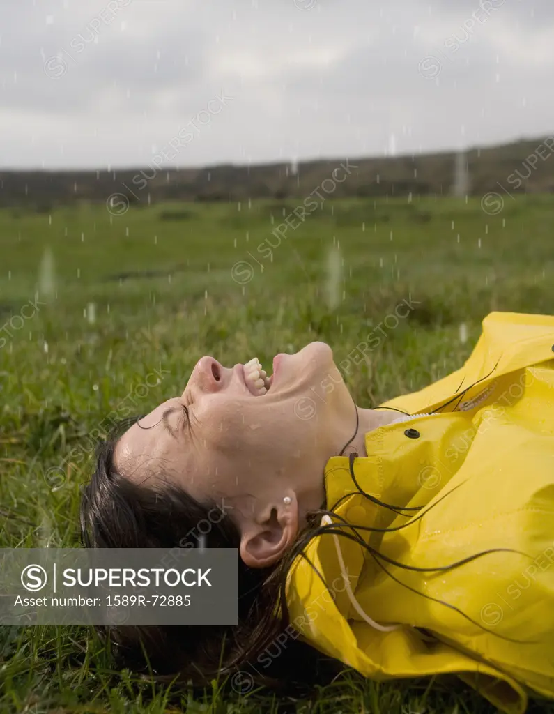 Hispanic woman laying on grass in rain