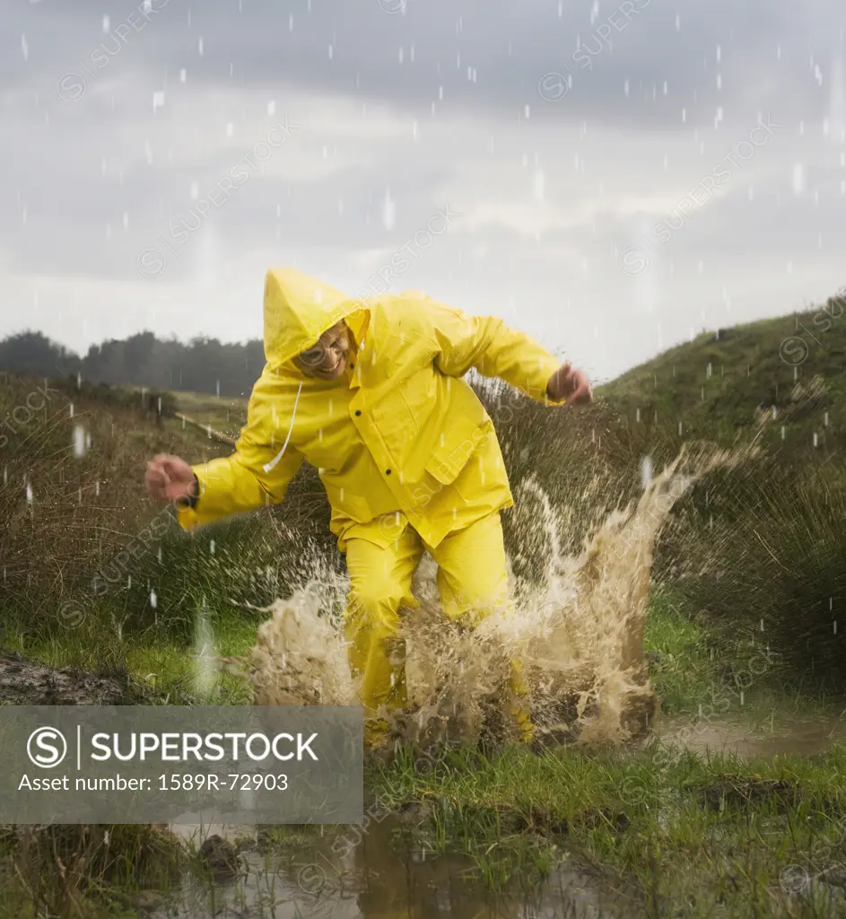 Hispanic man in rain gear jumping in puddle