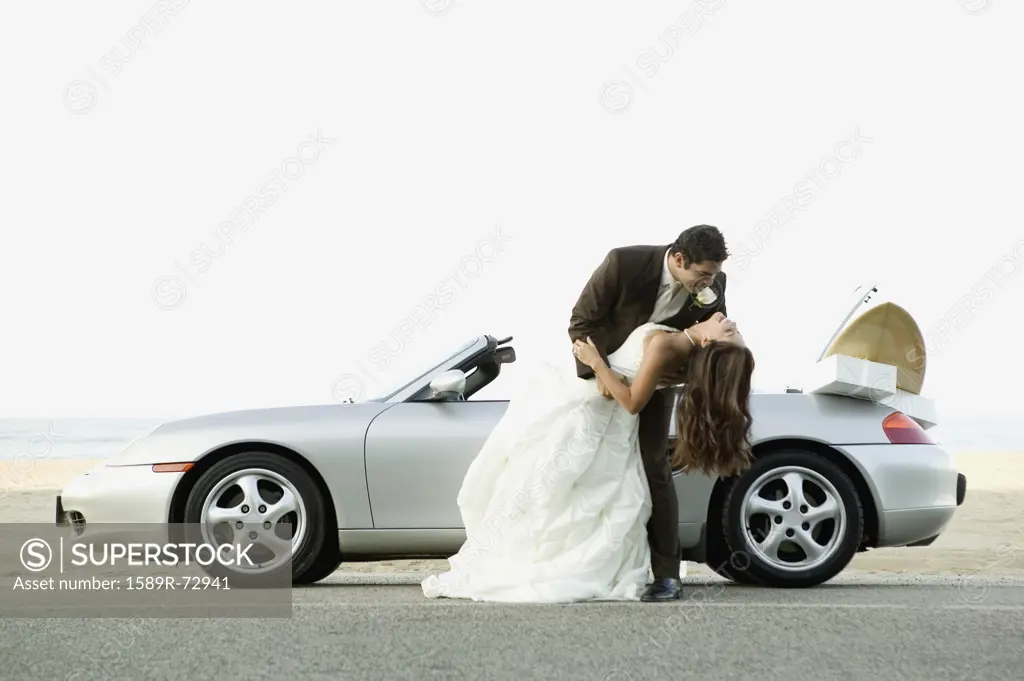 Hispanic newlyweds hugging next to car