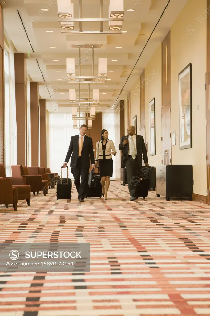 Multi-ethnic business people walking with suitcases in hotel