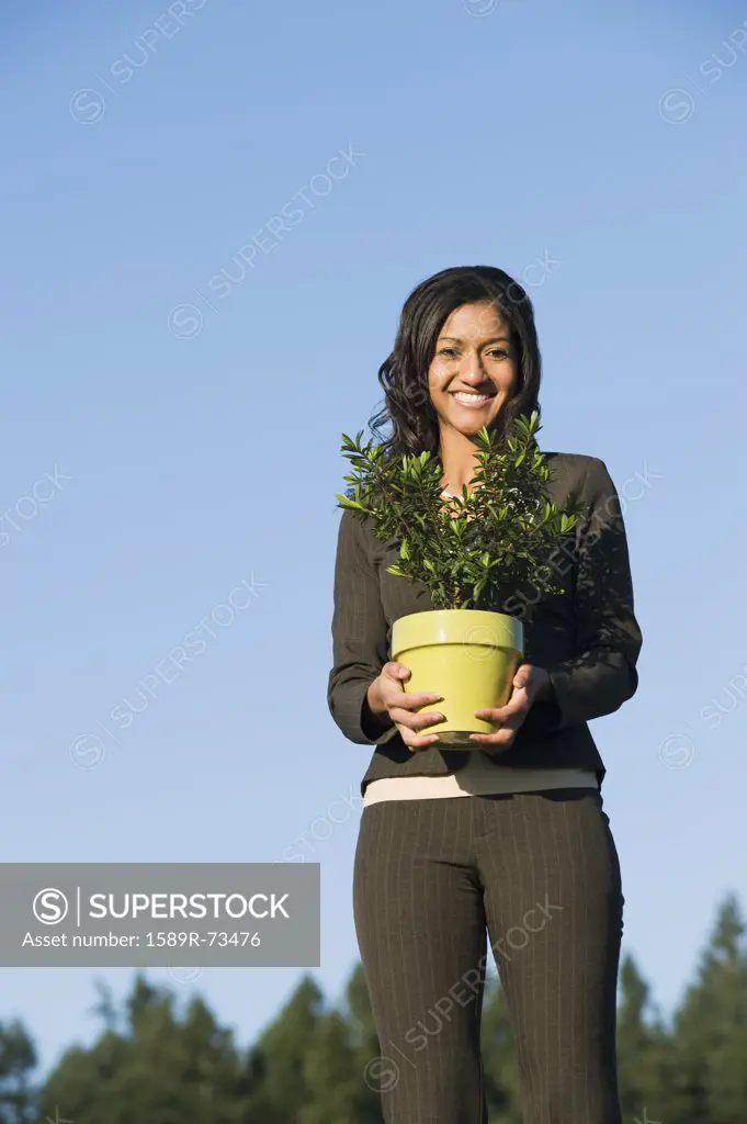 Mixed race businesswoman holding potted plant