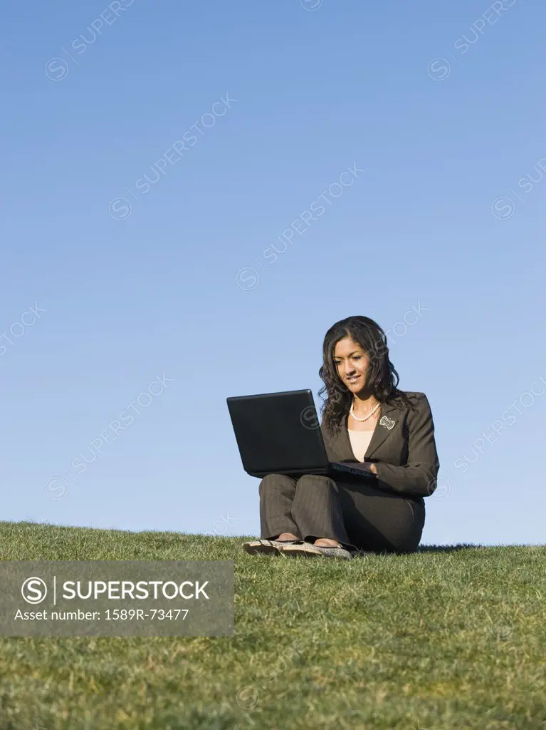 Mixed race businesswoman using laptop in grass