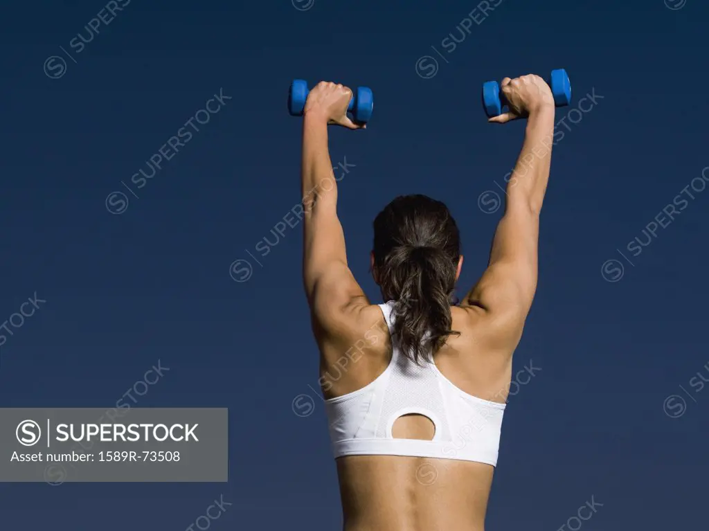 Rear view of mixed race woman holding dumbbells overhead