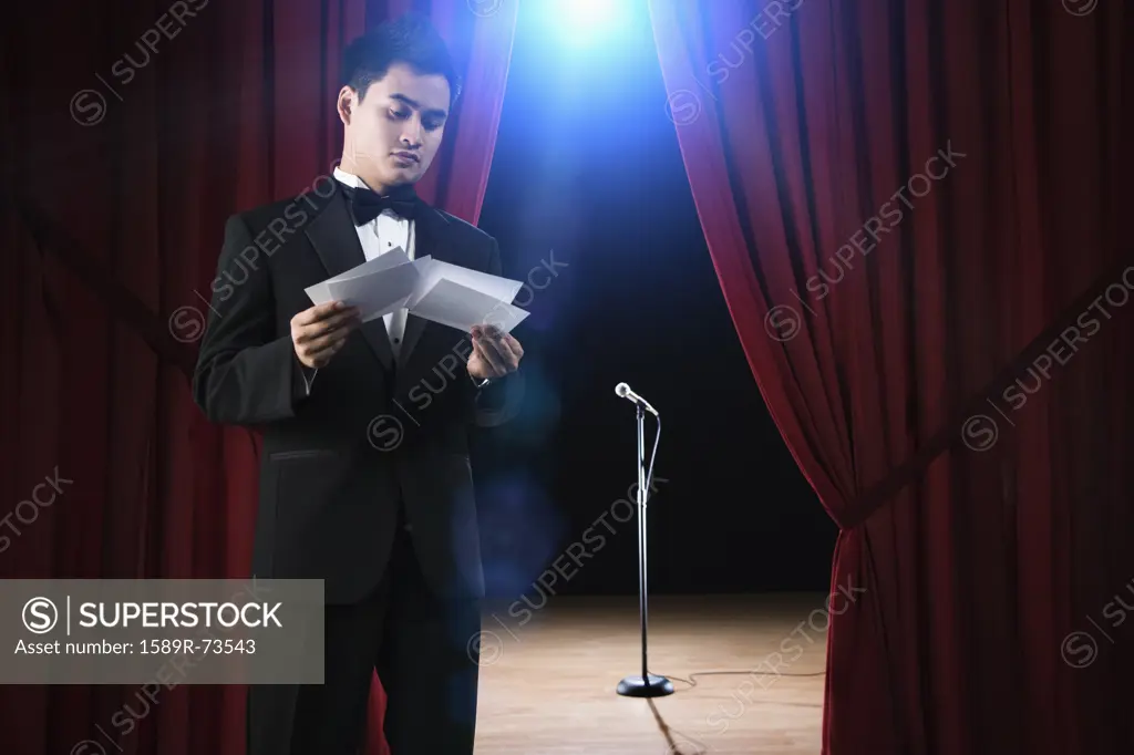 Asian man in tuxedo reviewing notecards backstage
