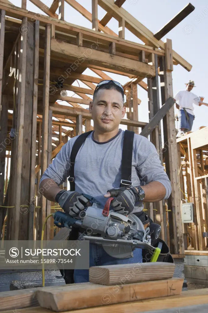 Hispanic man holding power saw at construction site