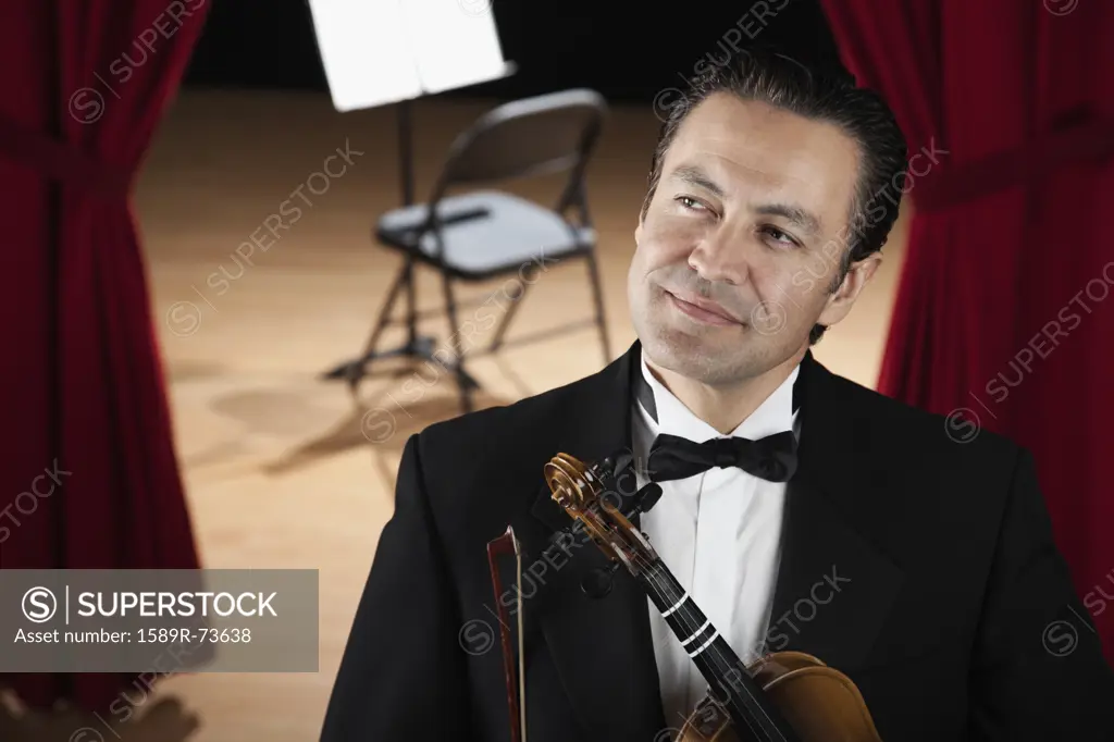 Hispanic man in tuxedo holding violin and looking pensive