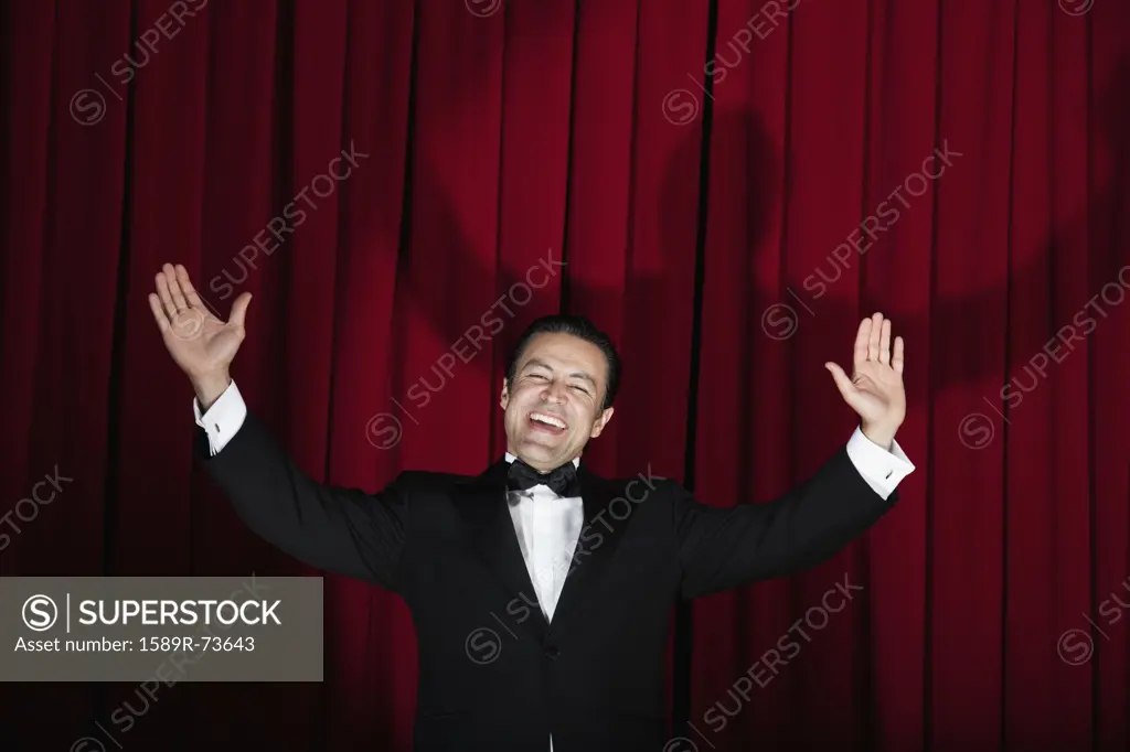 Hispanic man in tuxedo singing with arms outstretched onstage