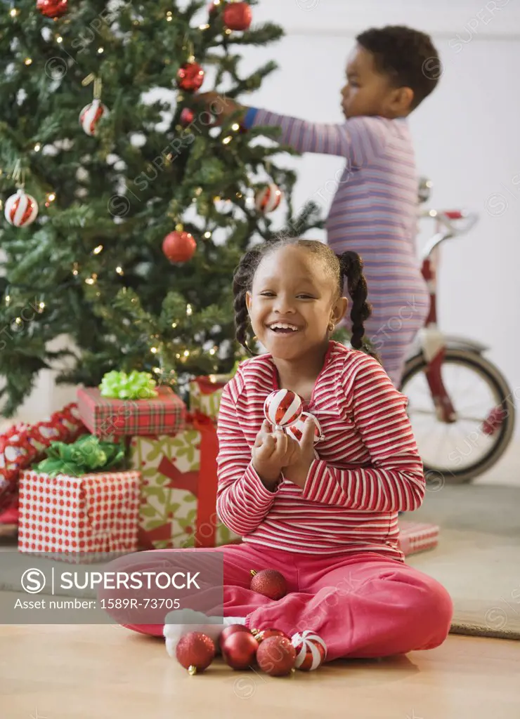 African American girl holding ornaments near Christmas tree