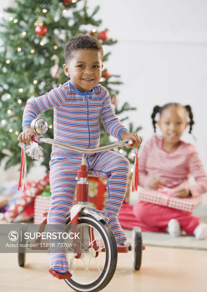 African American boy riding tricycle near Christmas tree
