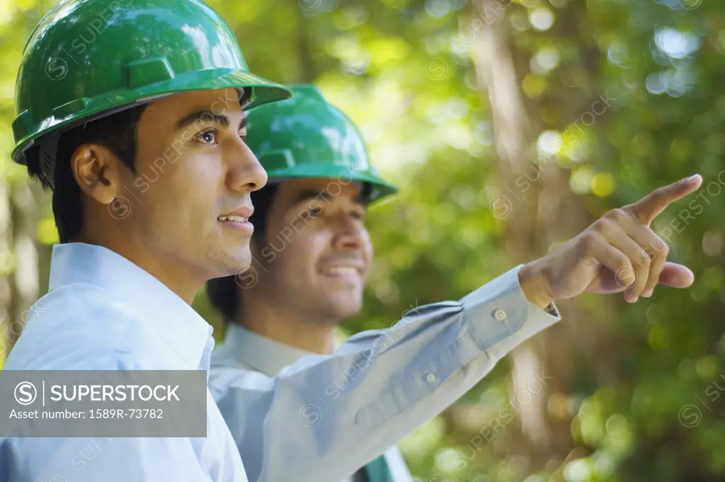 Hispanic businessmen in green hard hats pointing outdoors