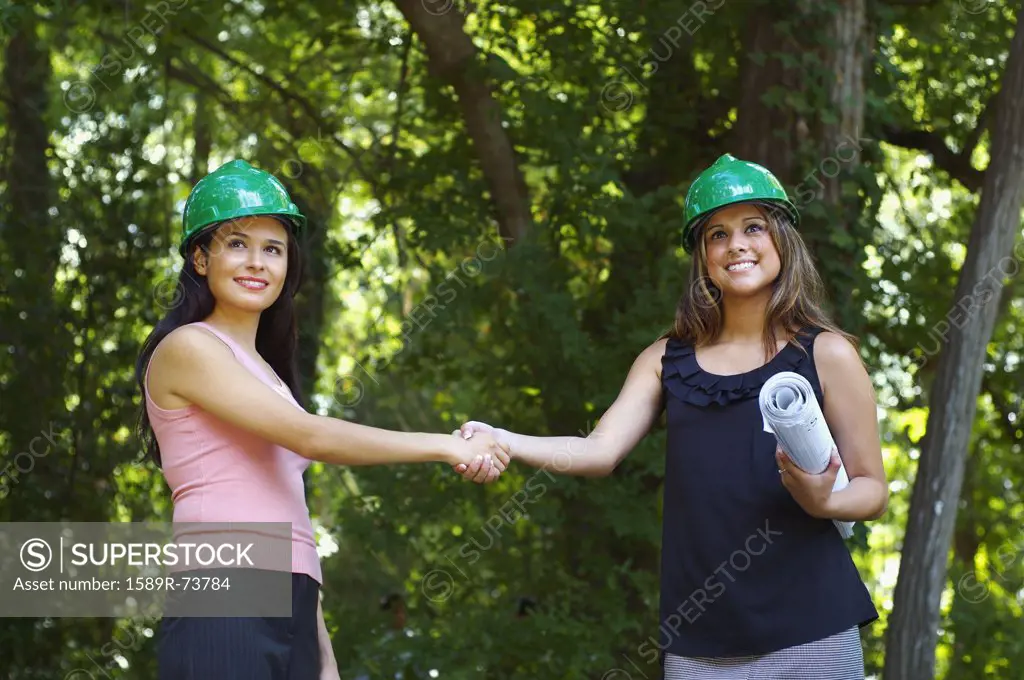 Hispanic architects in green hard hats shaking hands outdoors