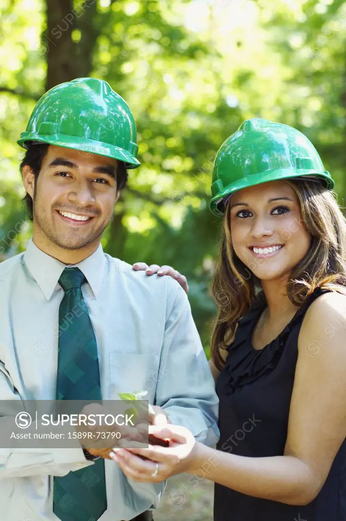 Hispanic business people with green hard hats holding tree sprout