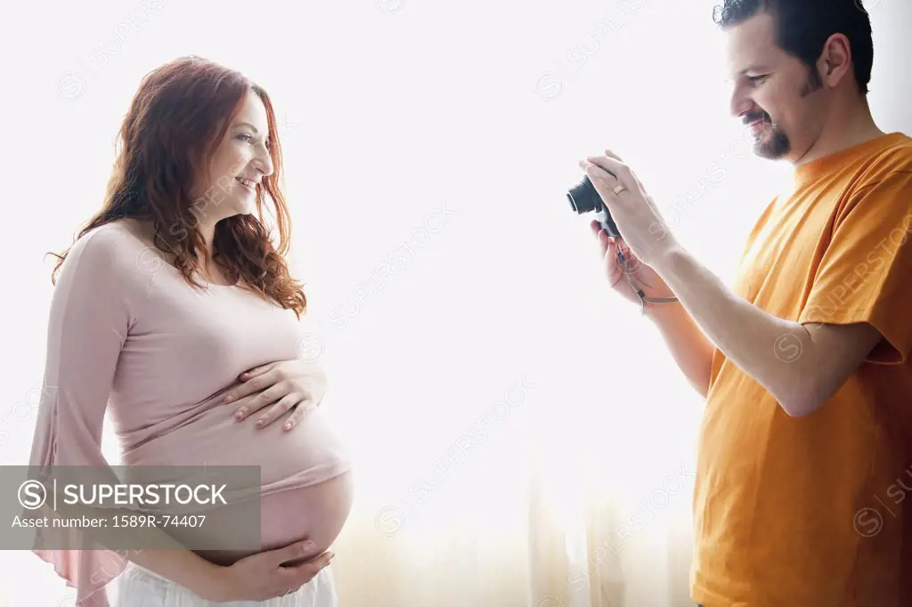 Hispanic man taking photograph of pregnant wife