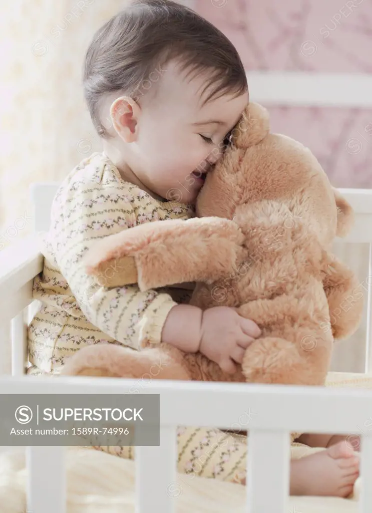 Mixed race baby girl snuggling teddy bear