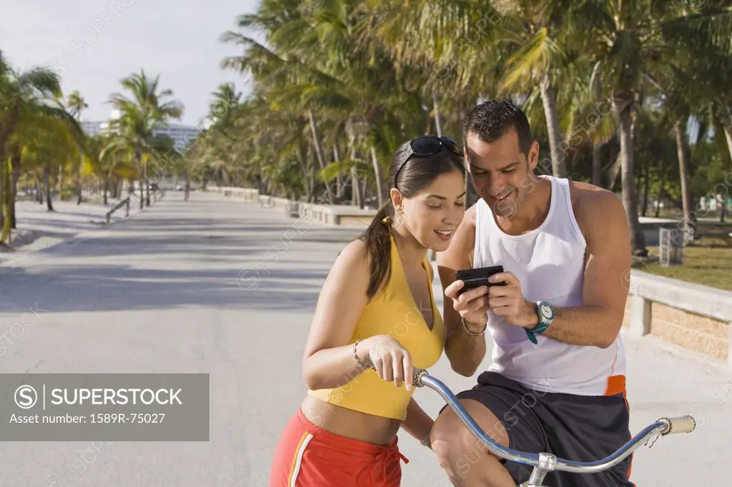 Hispanic couple on bicycles looking at cell phone
