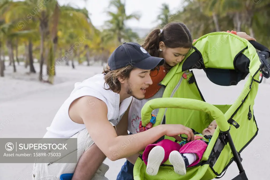 Hispanic father and daughter checking on baby in stroller