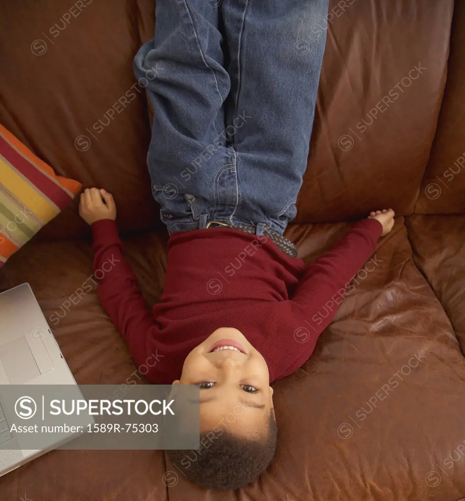 Mixed race boy laying upside down on couch