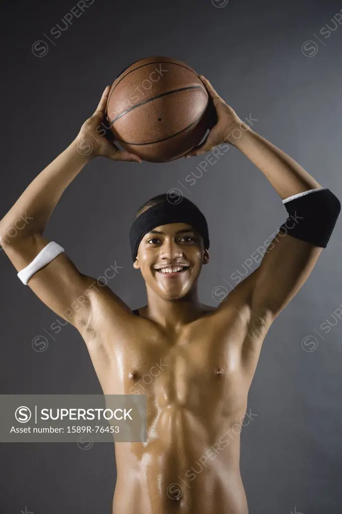 Mixed race basketball player holding ball overhead