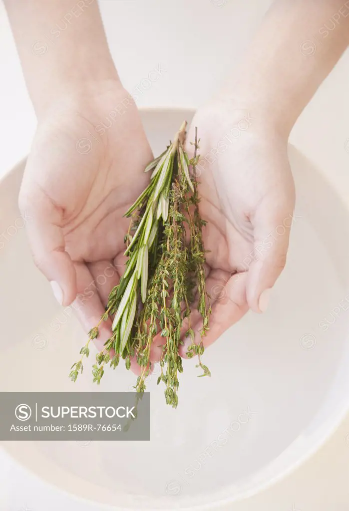 Woman holding fresh herbs over bowl of water