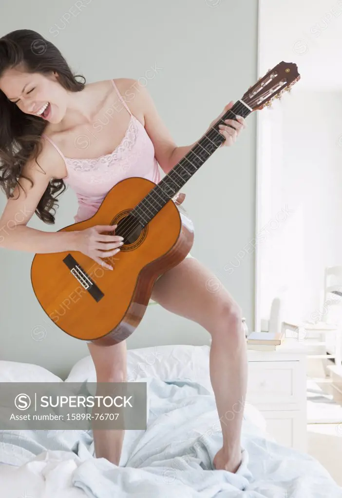 Mixed race woman playing guitar on bed