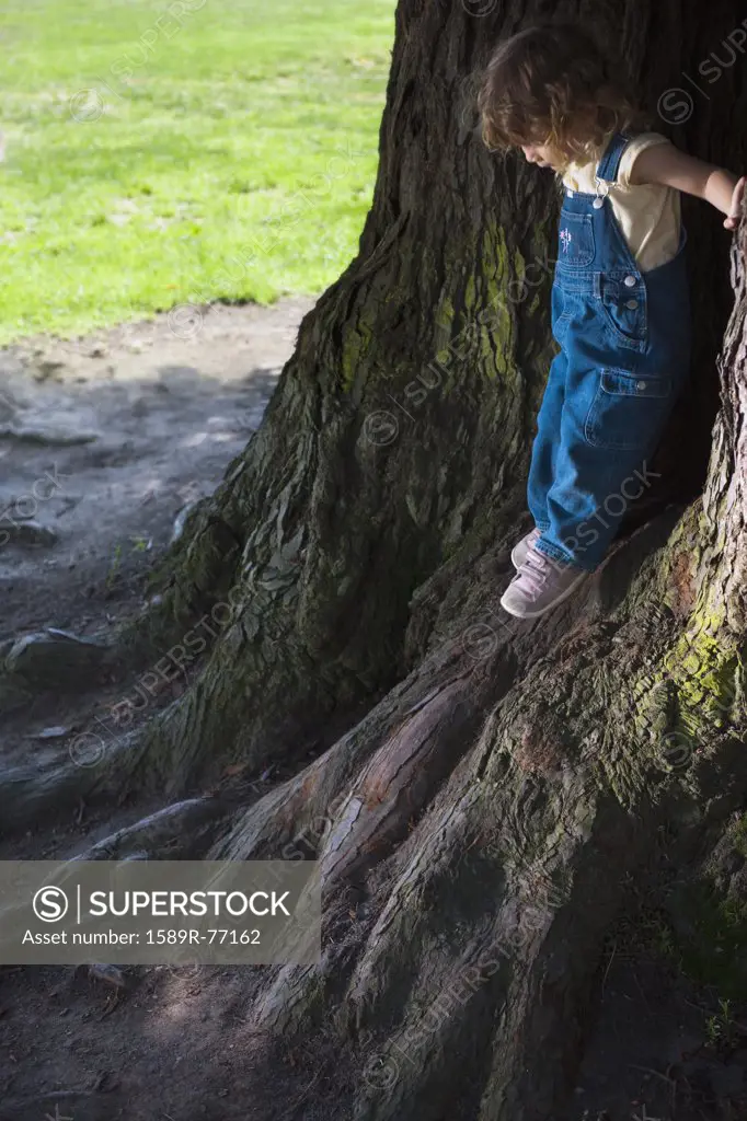 Mixed race girl leaning on tree trunks