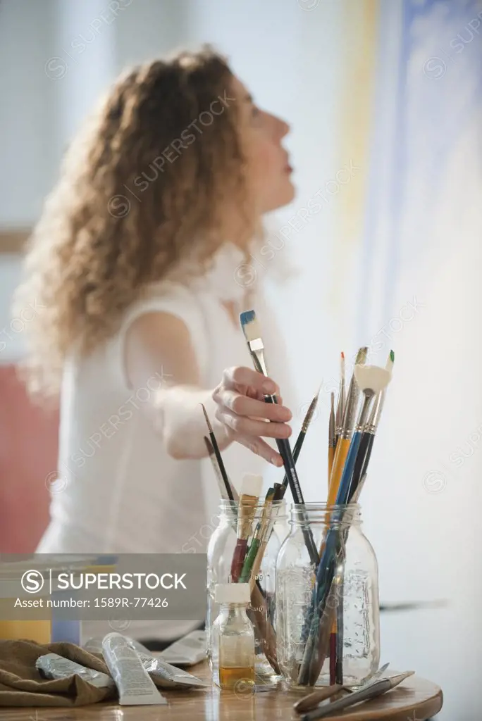 Hispanic woman reaching for paintbrush
