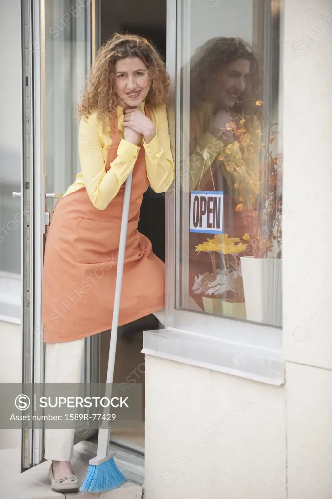 Hispanic shopkeeper holding broom in doorway