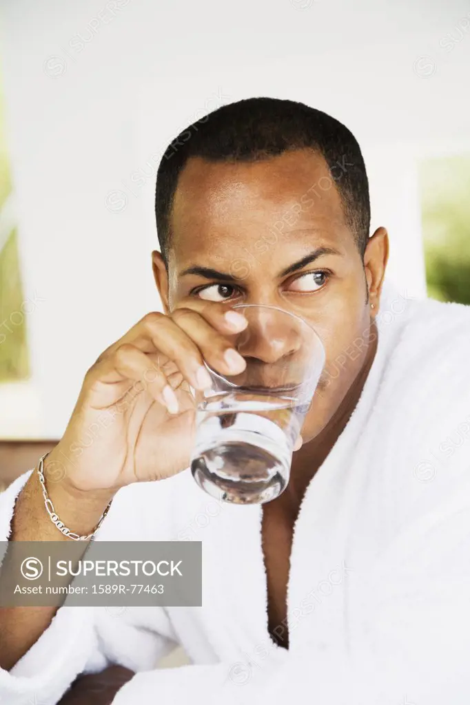 Mixed race man in bathrobe drinking water