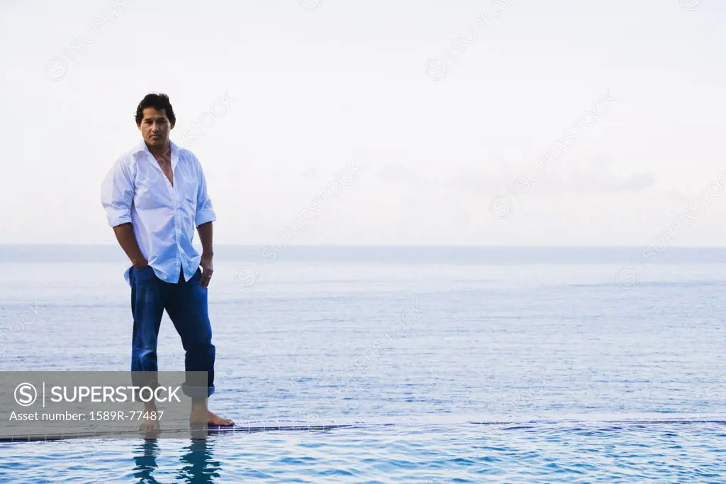 Mixed race man standing on edge of infinity pool
