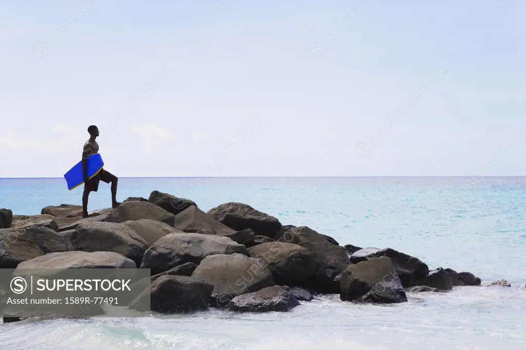African man holding body board on rocks in ocean