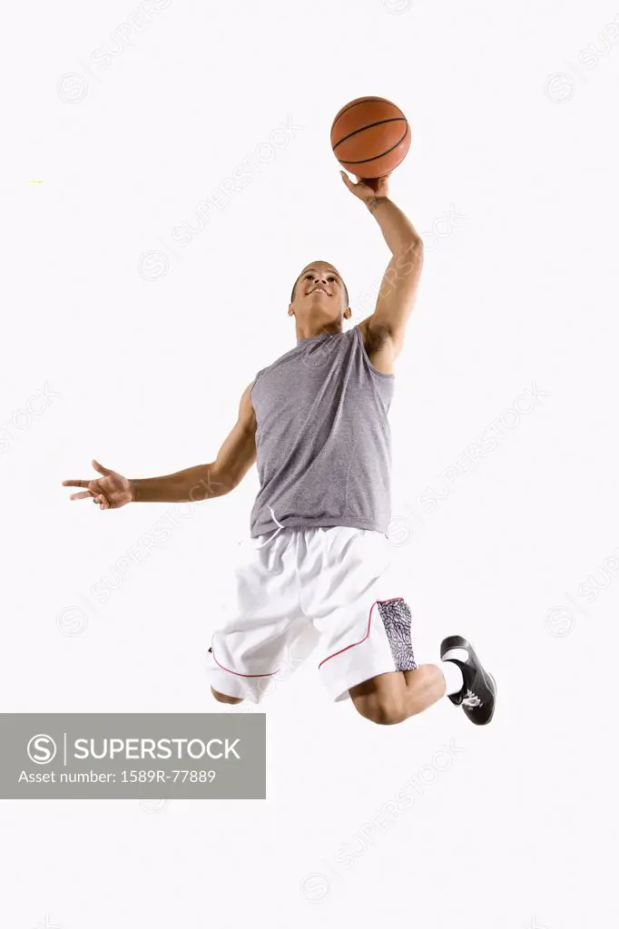 Mixed race basketball player jumping with ball