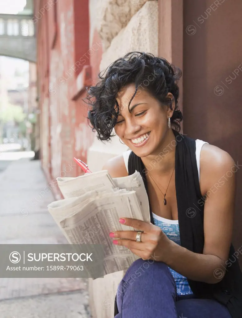 Mixed race woman reading classified ads on urban street