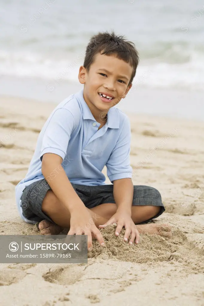 Mixed race boy playing with sand on beach
